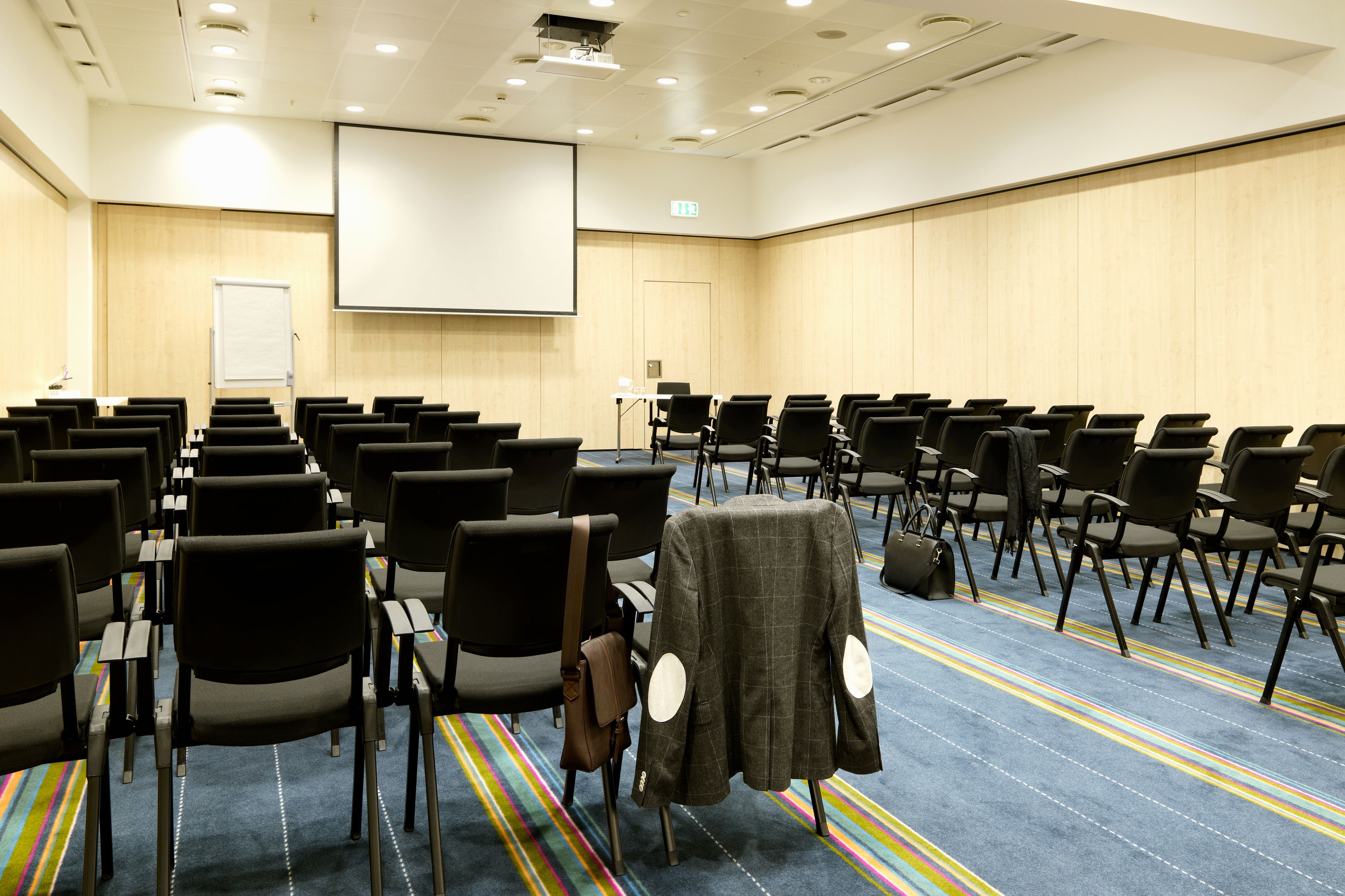 A conference room with rows of chairs, a projector screen, and a carpeted floor.