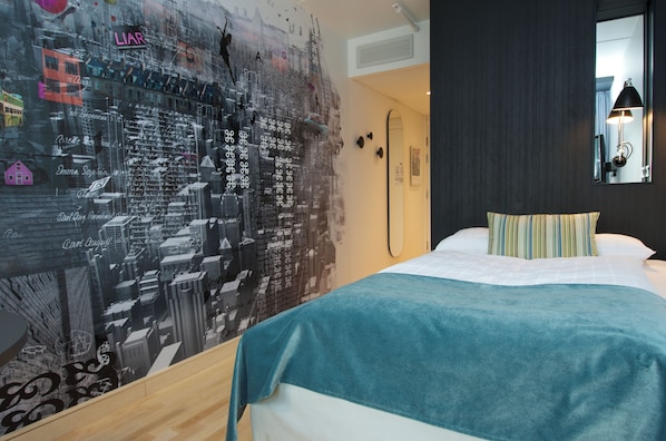 A hotel room with a bed, a cityscape mural, a mirror, and a door.