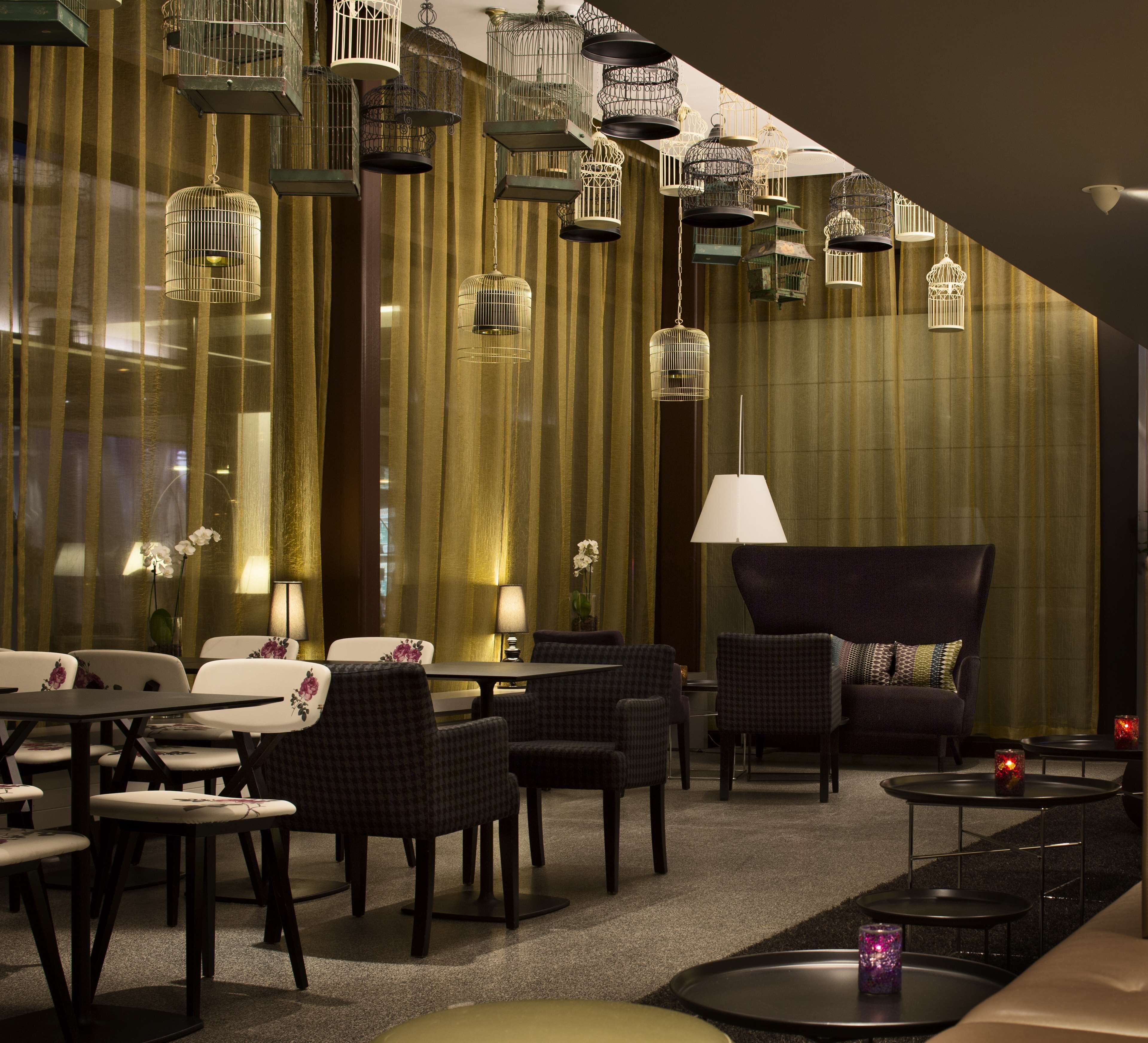 Ein stilvoller Lounge-Bereich mit gestaffelten Sitzgelegenheiten, hängenden Vogelkäfigen und stimmungsvoller Beleuchtung.
