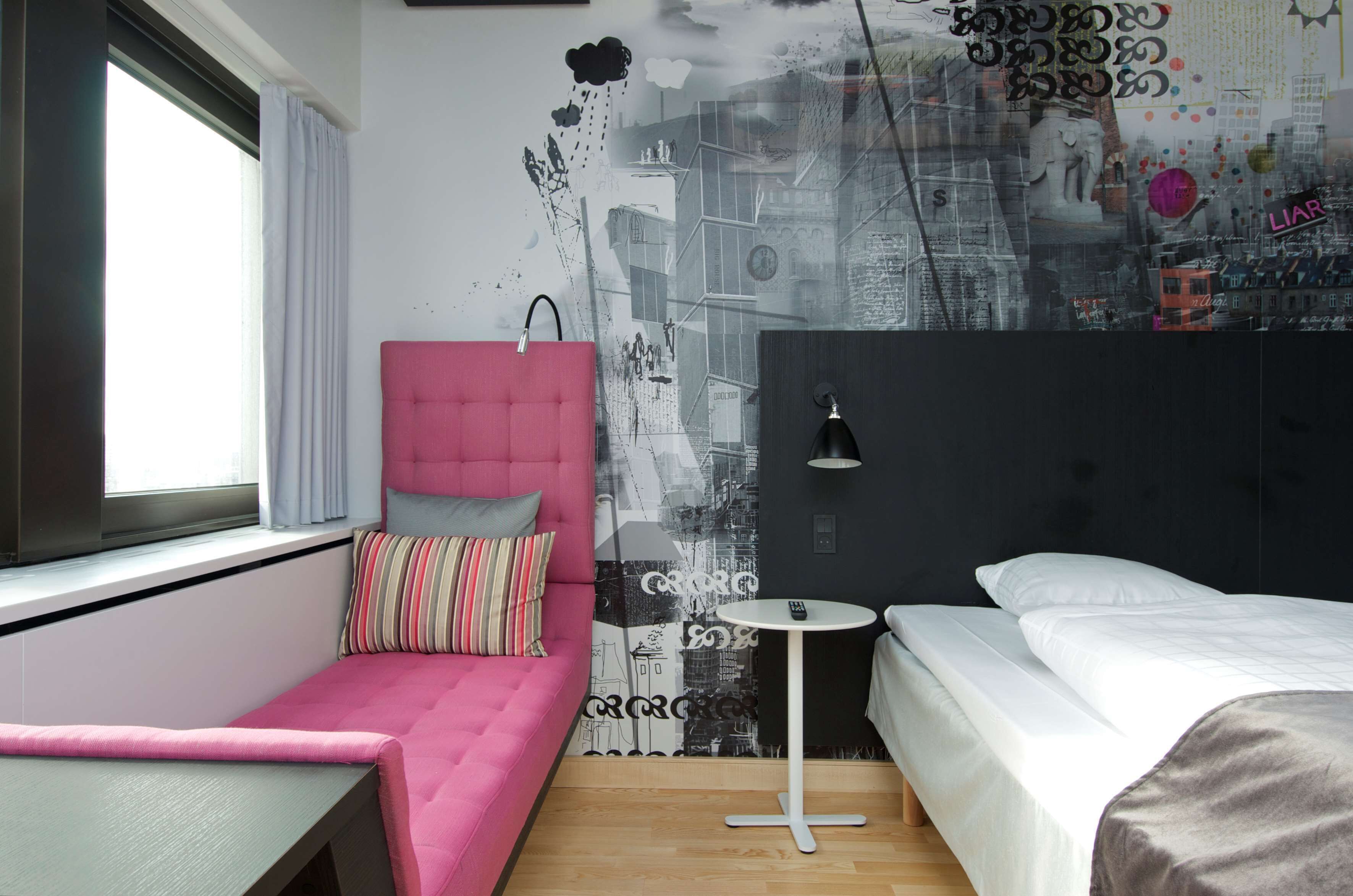 A modern bedroom with a pink sofa, a small bedside table, and a bed with white bedding.