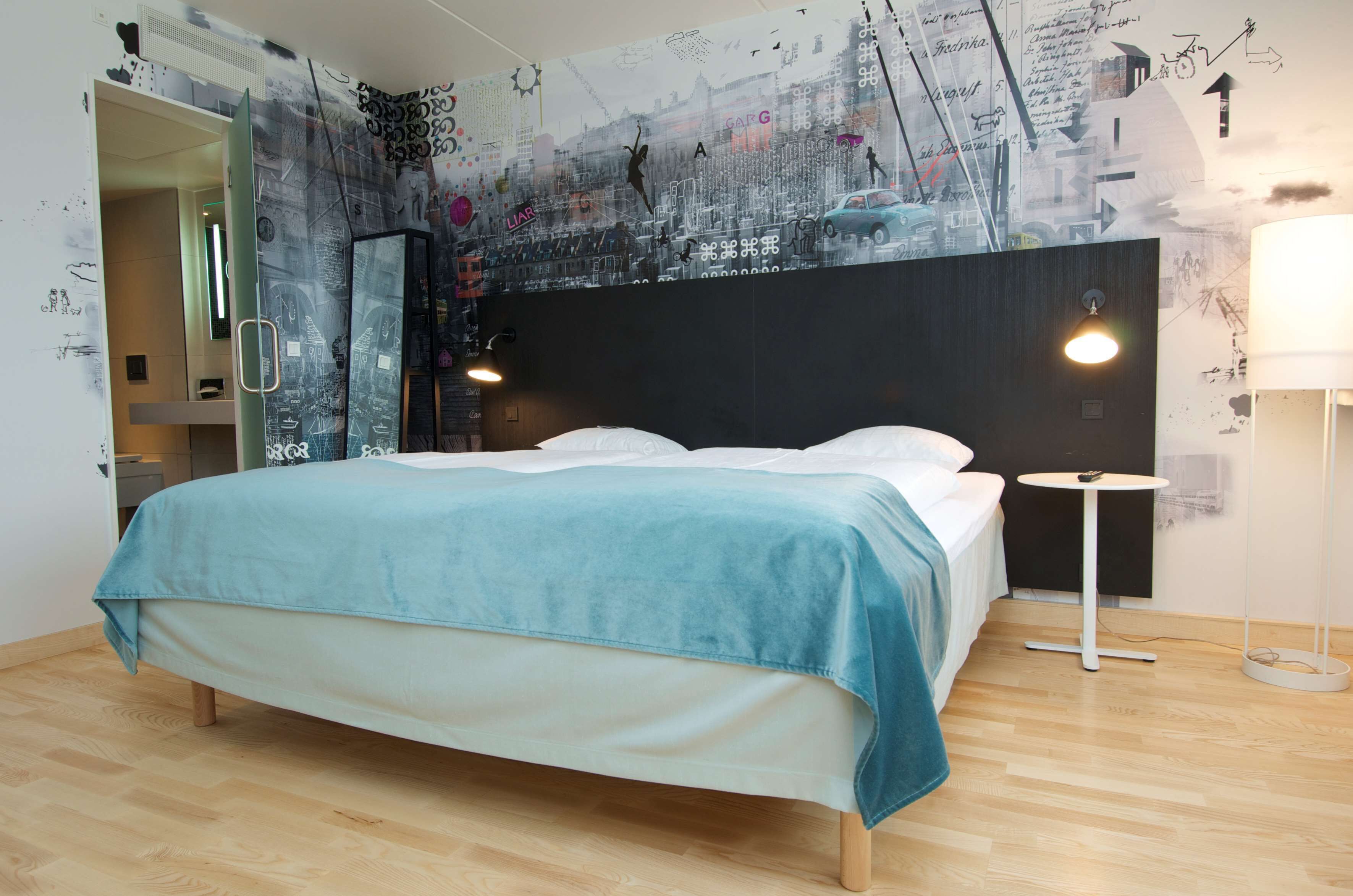 A modern bedroom with a bed, a nightstand, a wall-mounted lamp, and a mirror.