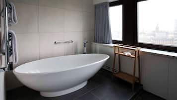 A modern bathroom with a freestanding bathtub, a towel rack, a window with a view of a cityscape, and a radiator.