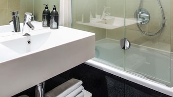 A modern bathroom with a white sink, chrome faucets, and a glass shower enclosure.