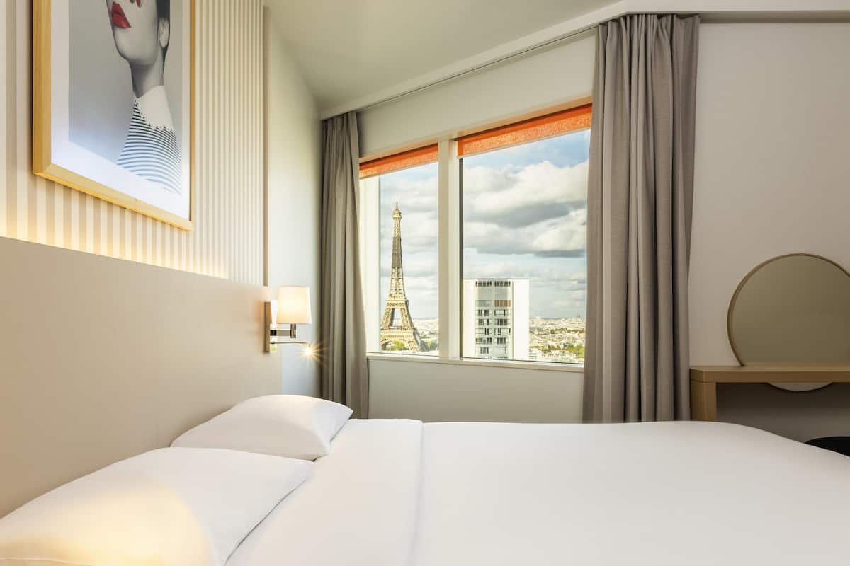 Habitación de hotel con una cama, vistas de la Torre Eiffel, una lámpara y un espejo en la pared.