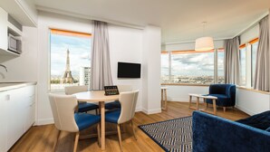 Una habitación de hotel moderna con zona de comedor, sofá, televisión y vistas a la Torre Eiffel.
