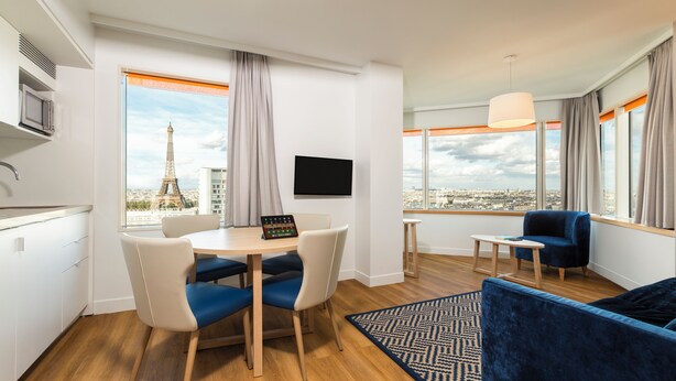 Una habitación de hotel moderna con zona de comedor, sofá, televisión y vistas a la Torre Eiffel.