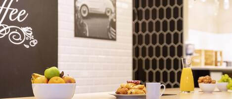 A breakfast table with a bowl of fruit, croissants, a coffee cup, and a glass of orange juice.
