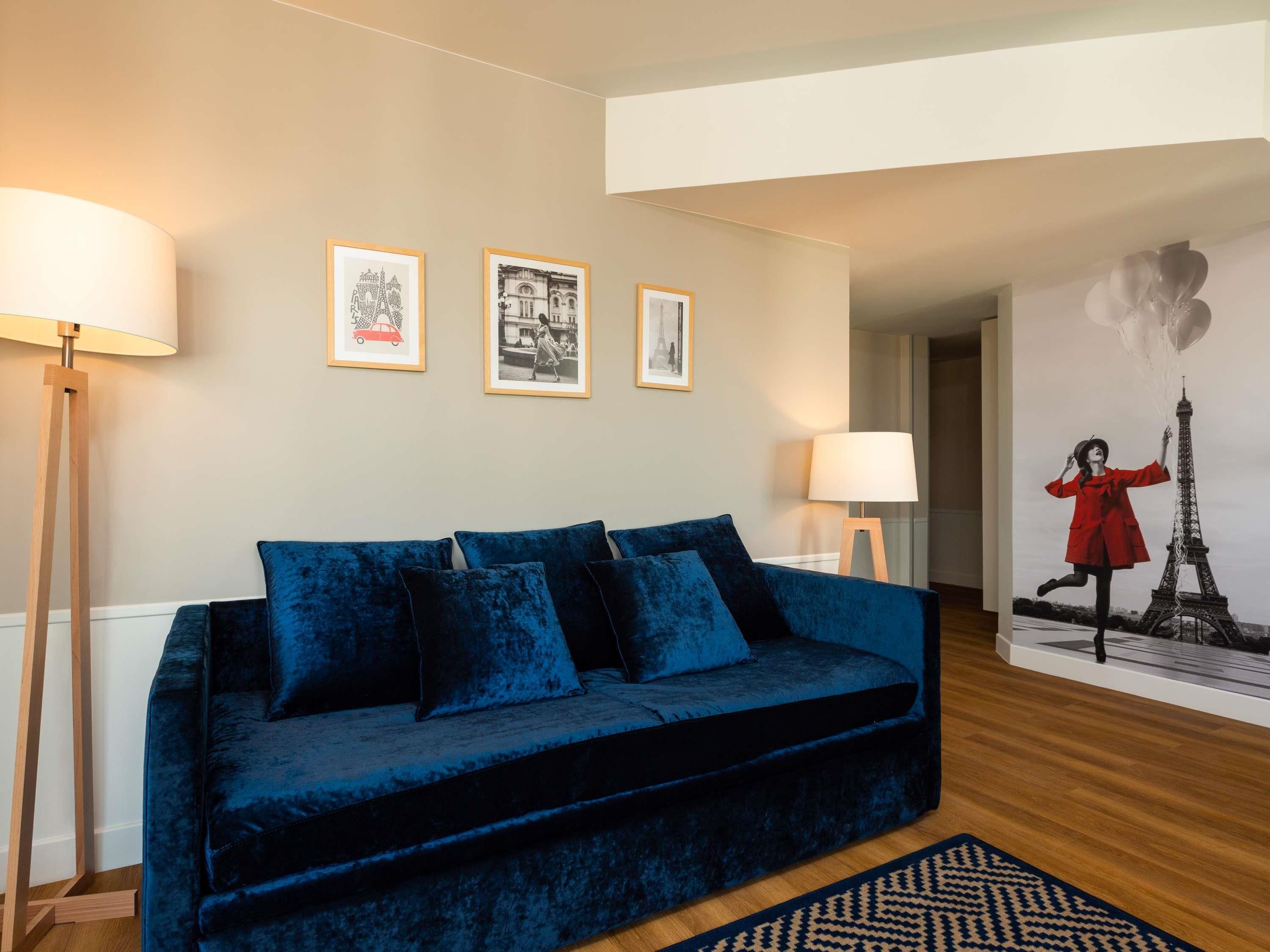 Una sala de estar con un sofá azul oscuro, dos lámparas de pie y tres cuadros en la pared.