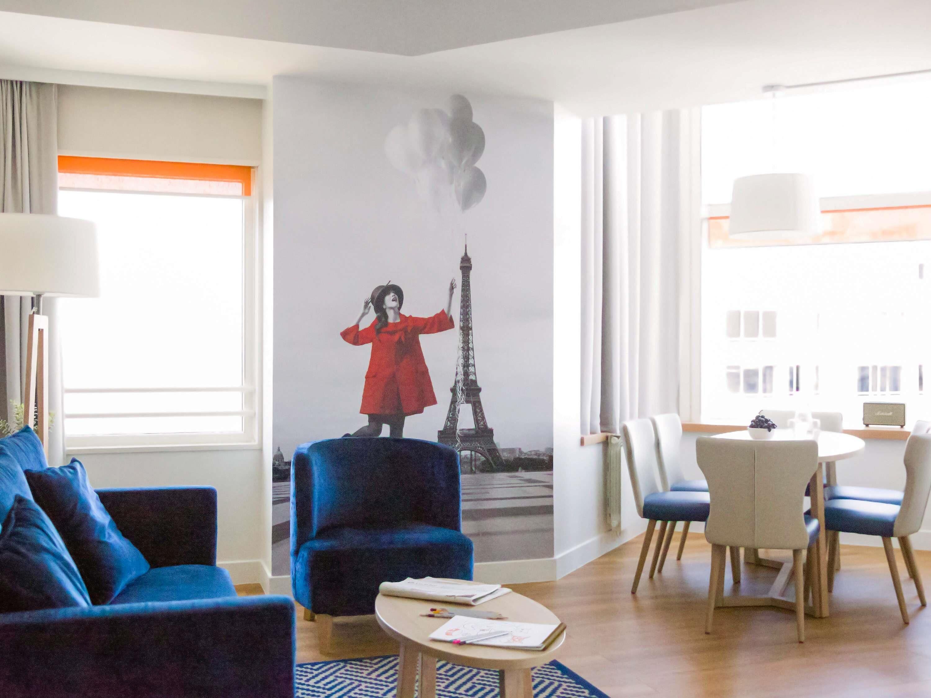 Een hotelkamer met een grote muurschildering van de Eiffeltoren, een blauwe bank, een eettafel met stoelen en een kleine salontafel.