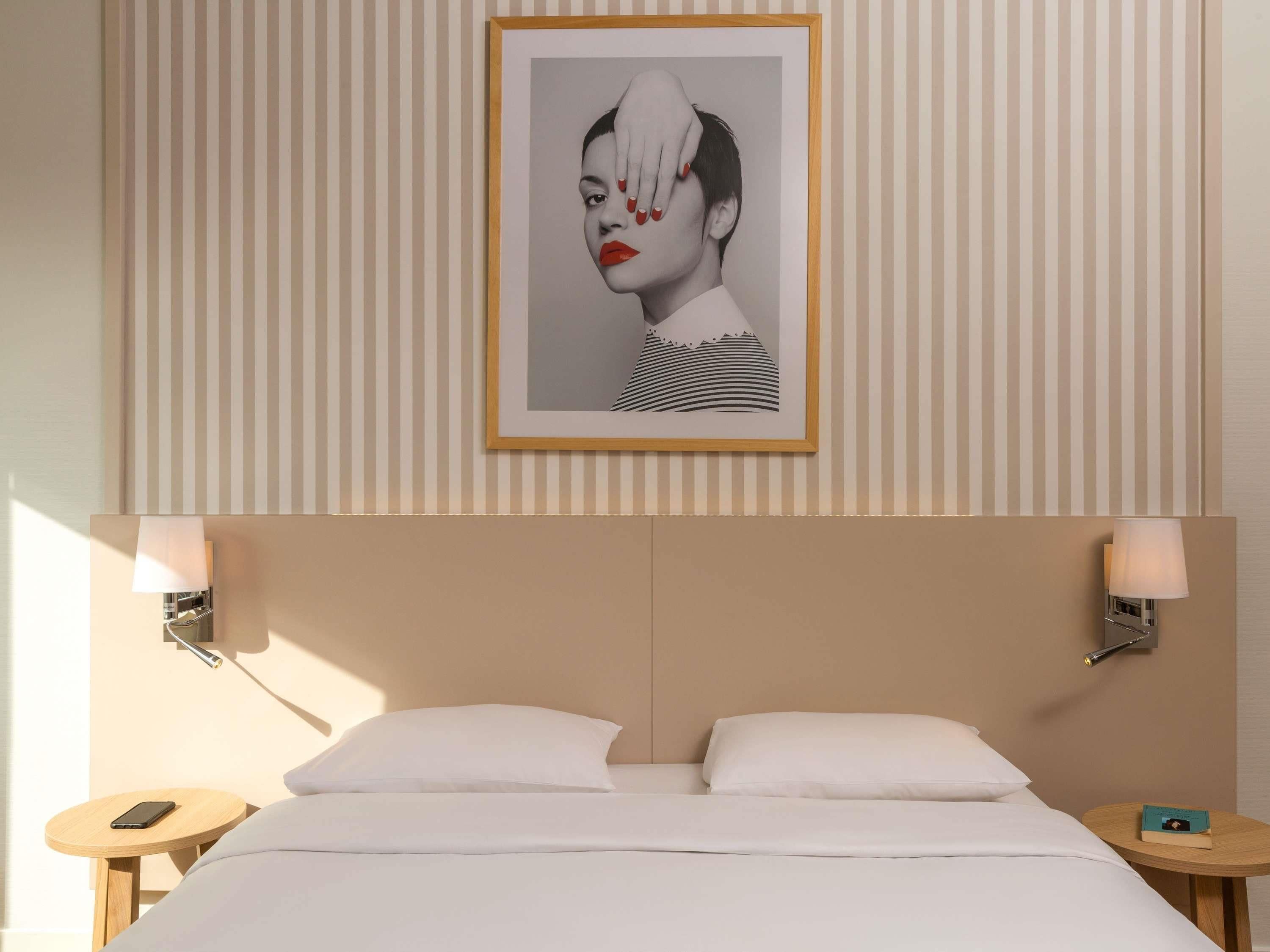 Habitación de hotel con una cama, dos mesitas de noche, un cuadro en la pared y un papel tapiz con estampado a rayas.