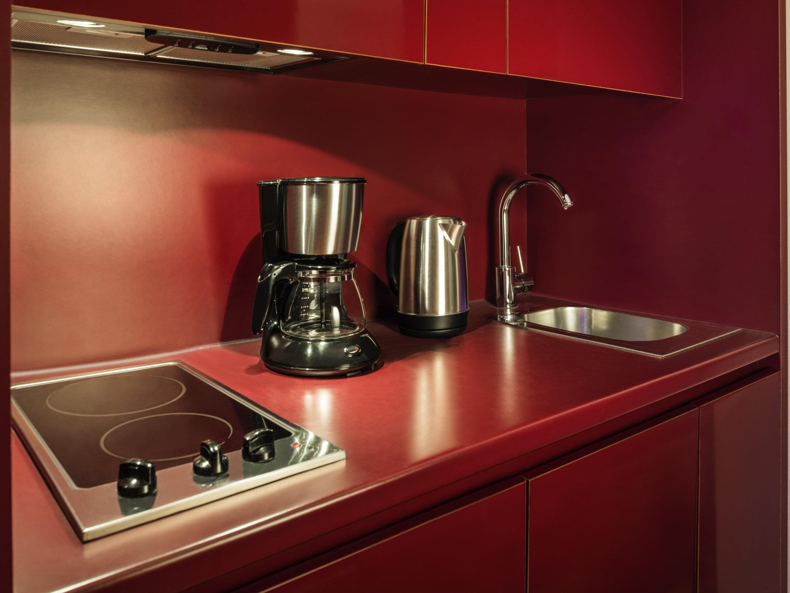 A modern kitchen with a built-in stovetop, a coffee maker, a kettle, and a stainless steel sink.