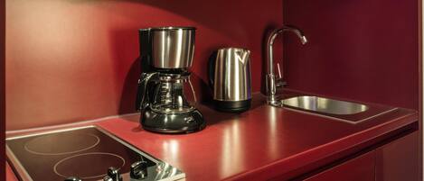 A modern kitchen with a built-in stovetop, a coffee maker, a kettle, and a stainless steel sink.