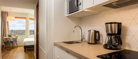 Habitación de hotel moderna con zona de cocina equipada con estufa, cafetera y hervidor.