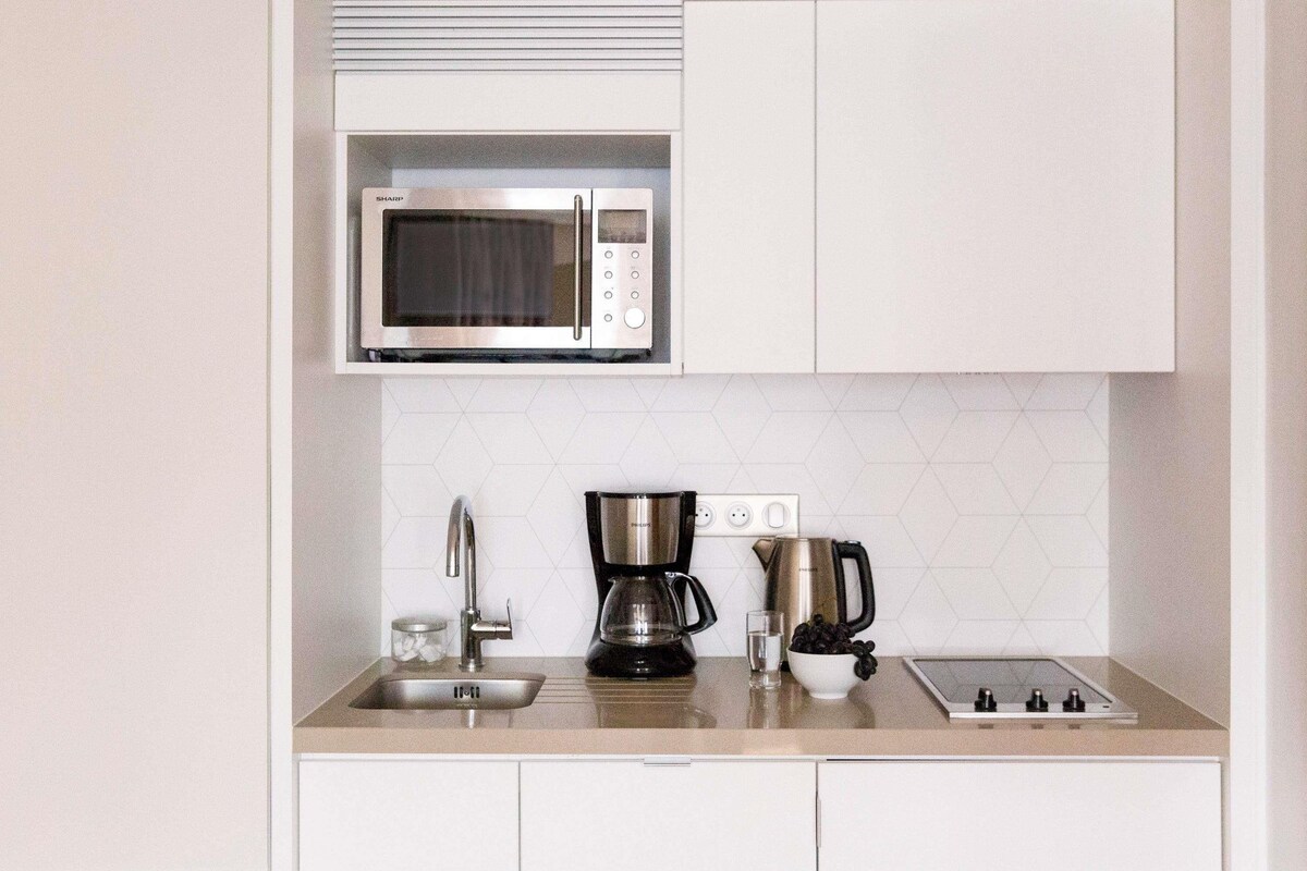 Cocina compacta con microondas integrado, cafetera, hervidor y pileta.