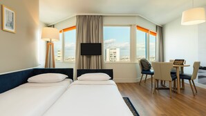 Una habitación de hotel con dos camas, televisión, escritorio con sillas y una ventana grande con cortinas.