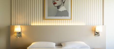 Una habitación de hotel con una cama grande, dos mesitas de noche, una obra de arte enmarcada sobre la cama y lámparas fijadas a la pared.