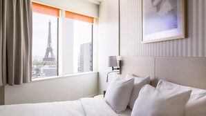 Una habitación de hotel con cama, ventana con cortinas, lámpara de pared y un cuadro enmarcado.