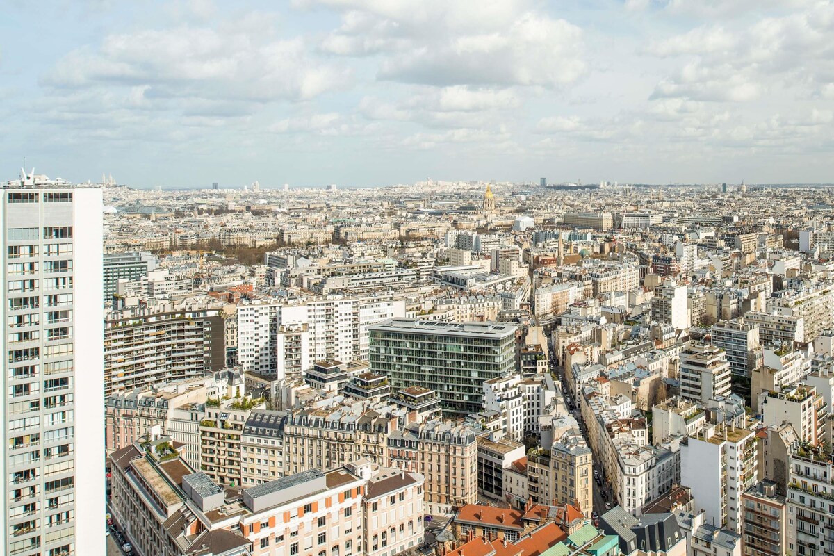 Paesaggio urbano con edifici densi, un moderno edificio in vetro ben visibile e un grande grattacielo bianco.