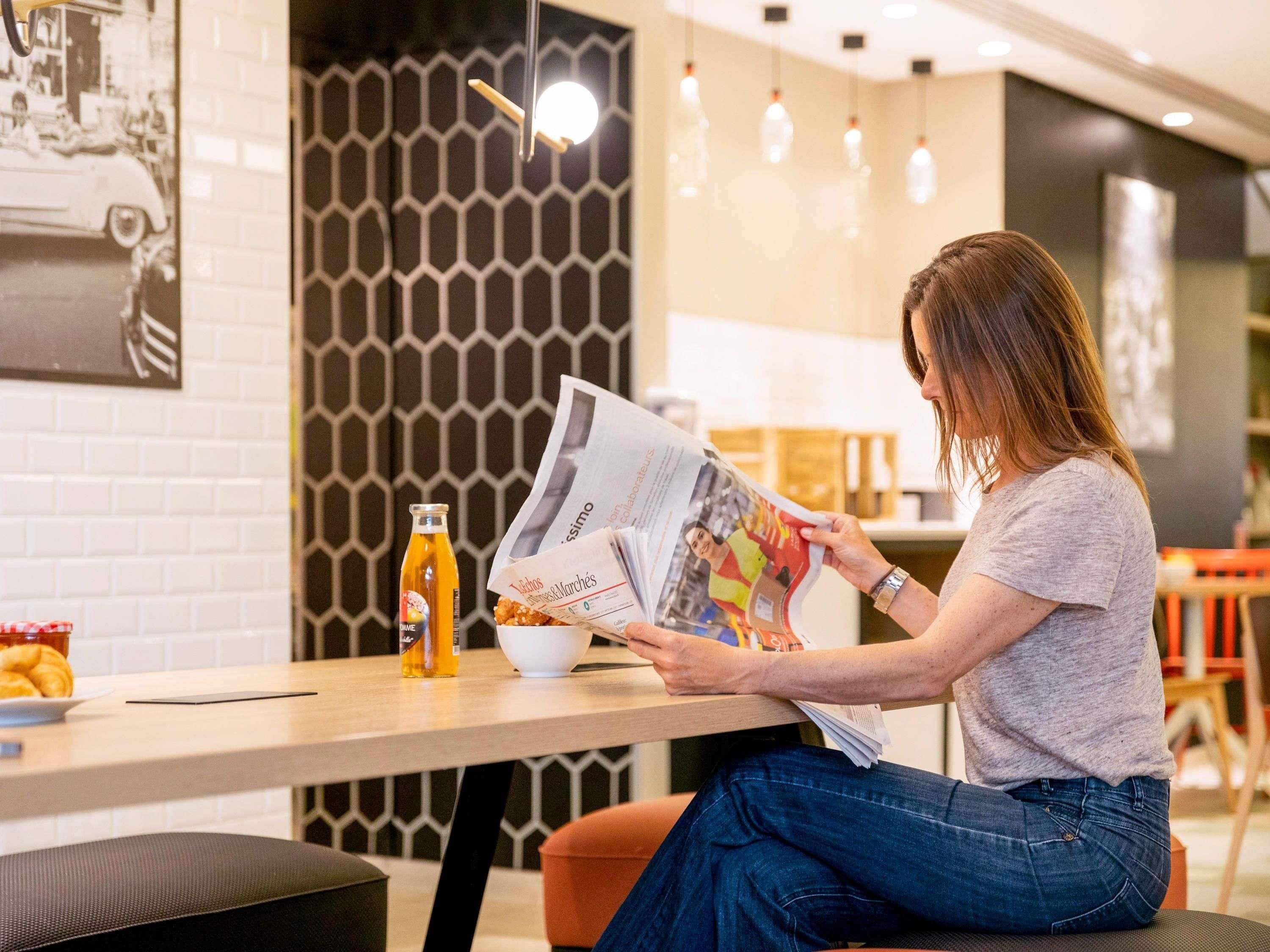 Una persona leyendo una revista en una mesa con una botella y un plato de comida.