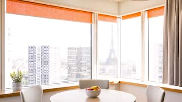A modern hotel room with a round table and chairs, large windows with orange blinds, and a view of the Eiffel Tower.