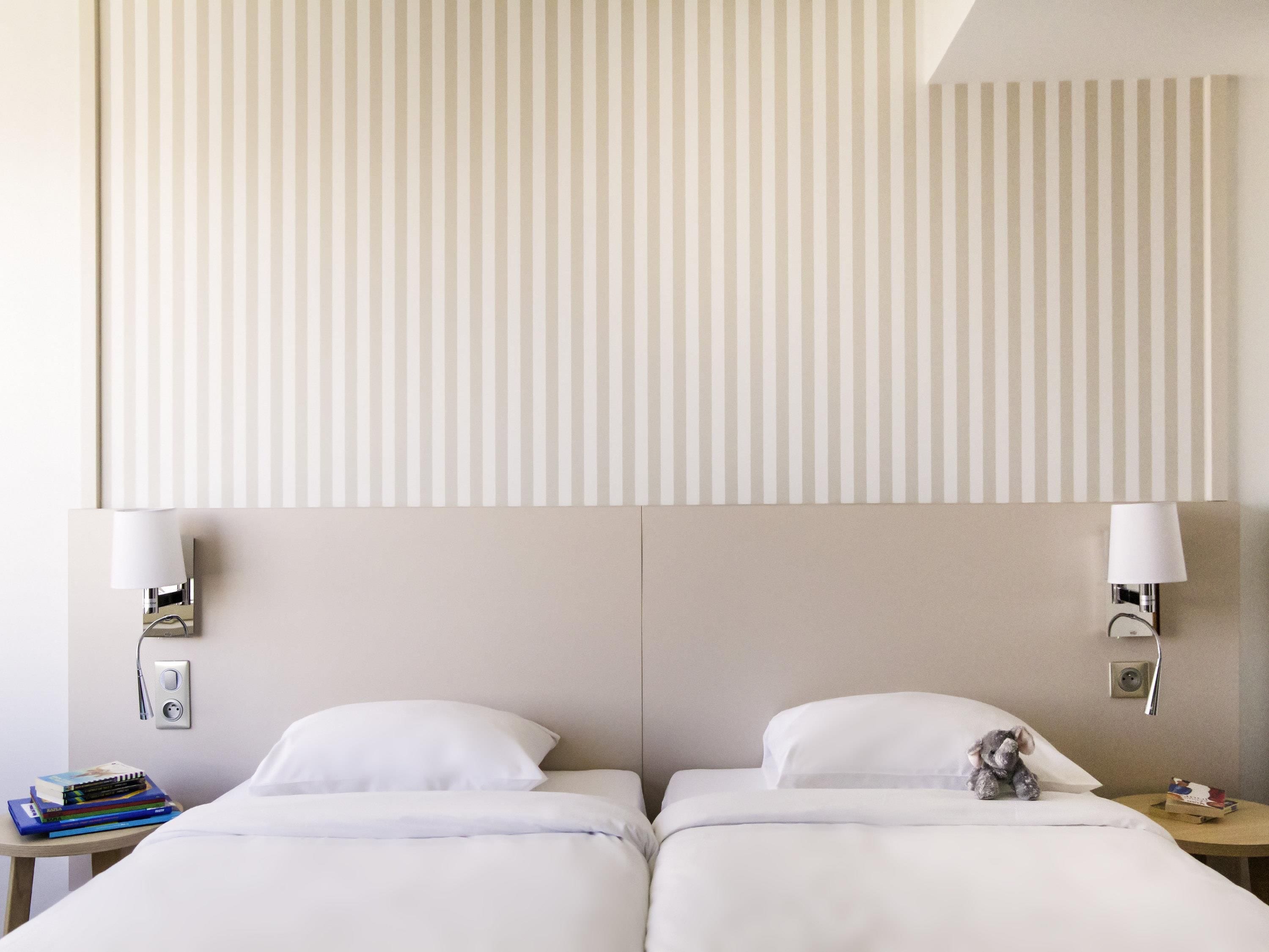 Une chambre d’hôtel avec deux lits, une table de chevet avec une lampe et un luminaire fixé au mur.