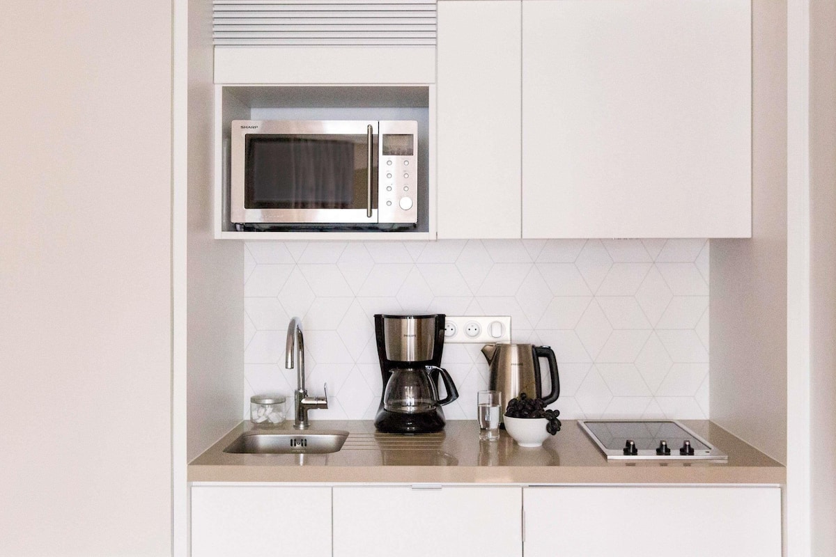 Cocina compacta con microondas integrado, cafetera, hervidor y pileta.