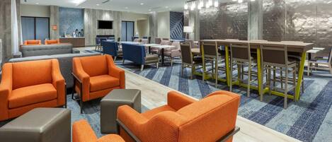 Un hall d’hôtel avec des sièges orange, un espace repas et un écran de télévision.