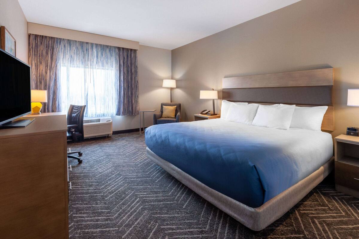A hotel room with a large bed, a desk, a chair, a TV, and a window with curtains.