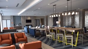 A modern hotel lobby with a large dining area, comfortable seating, and a flat-screen TV mounted on the wall. - La Quinta Inn & Suites by Wyndham Middletown-Goshen (Middletown)
