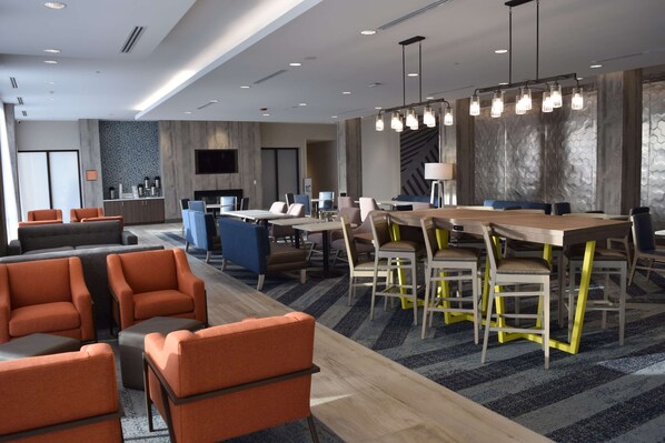 A modern hotel lobby with a large dining area, comfortable seating, and a flat-screen TV mounted on the wall. - La Quinta Inn & Suites by Wyndham Middletown-Goshen (Middletown)