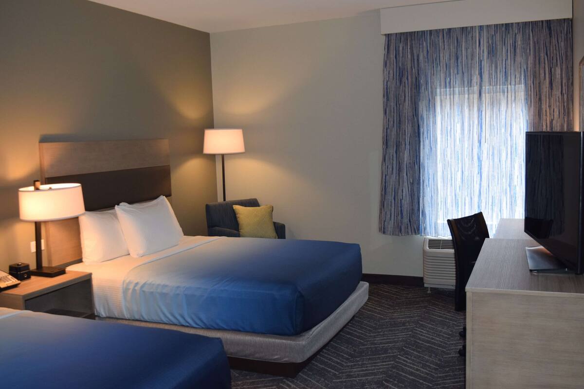 A hotel room with two beds, a desk, a chair, a TV, and a window with curtains.