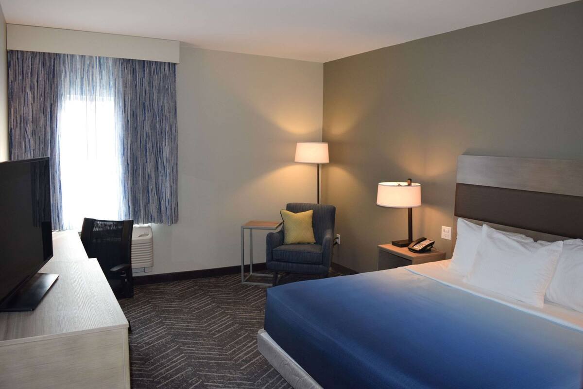 A hotel room with a bed, a desk, a chair, two lamps, and a television.