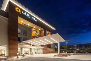 A hotel entrance with a covered walkway, a prominent sun logo, and a modern facade. - La Quinta Inn & Suites by Wyndham Middletown-Goshen (Middletown)