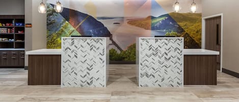 Zona de recepción de diseño moderno, con un mural grande en la pared, dos mostradores con fondos estampados y un área de almacenamiento con estanterías a la izquierda.