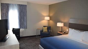 Habitación de hotel con cama, escritorio, laptop, silla, lámpara y televisión.
