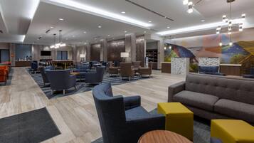 A modern hotel lobby with seating areas, a reception desk, and a large mural.