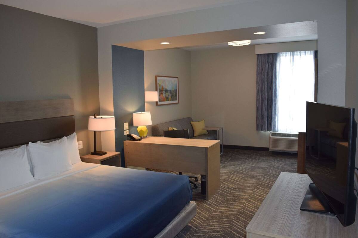 A hotel room with a bed, desk, chair, TV, lamp, and a painting on the wall.
