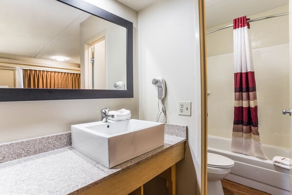 A bathroom with a white sink, a mirror, a hairdryer, and a shower curtain. - Red Roof Inn PLUS+ Nashville North - Goodlettsville (Goodlettsville)