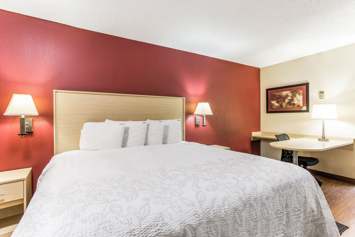 A hotel room with a large bed, two bedside lamps, a desk with a chair, and a small table.