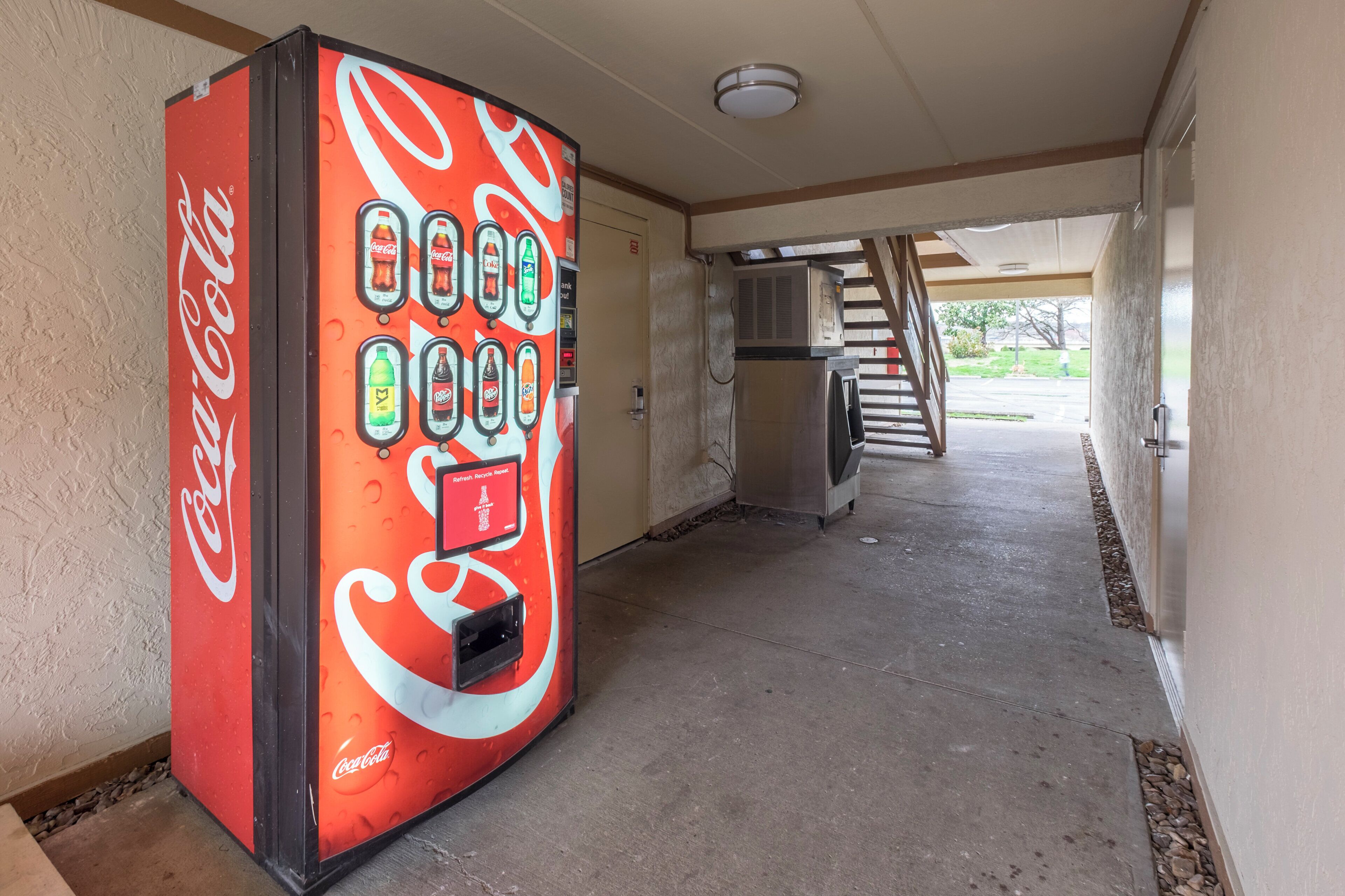 Eine Coca-Cola-Automat steht in einem Flur mit einer Treppe, die zu einem Außenbereich führt.