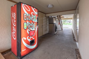 Una máquina expendedora de Coca-Cola en un pasillo con una escalera que lleva a un área exterior.