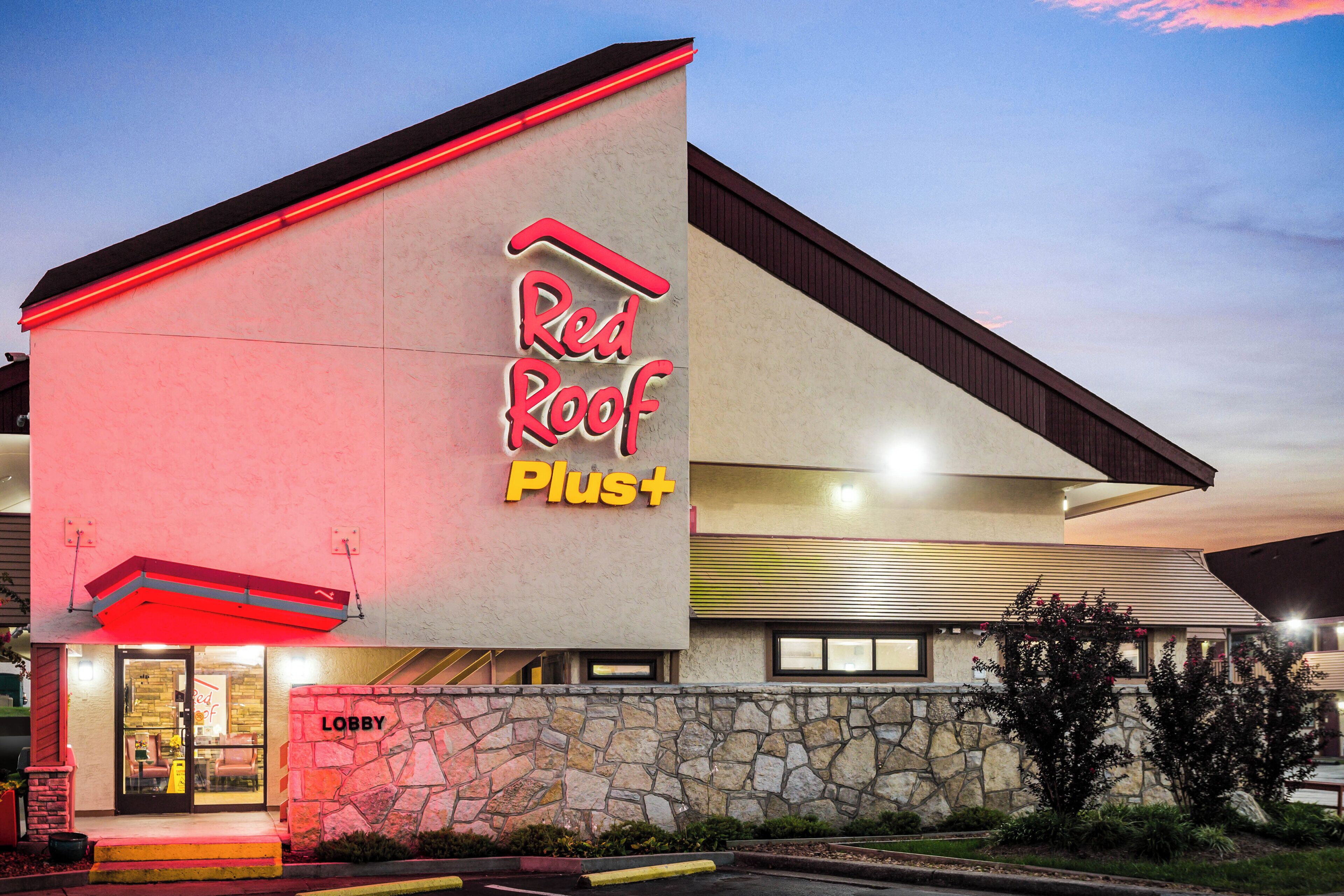 A building with a prominent 'Red Roof Plus' sign, a stone facade, and a visible entrance with a 'Lobby' sign.