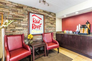 Cafetería Red Roof Plus+ con paredes de piedra, sillas de cuero, una mesa pequeña con un florero y una barra con dispensadores de café.