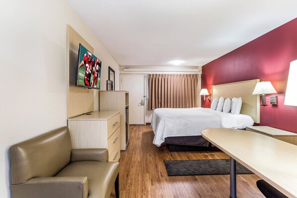 Una habitación de hotel con cama, escritorio, silla, televisor y armario.