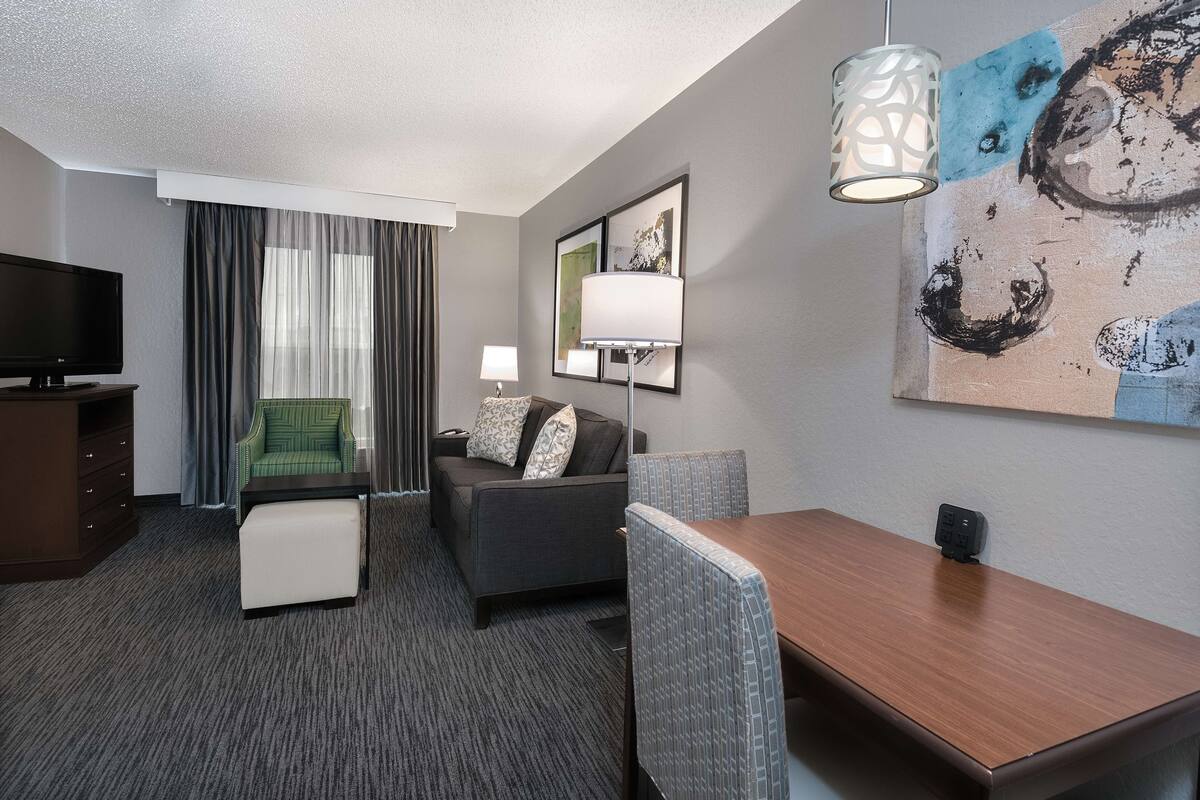 A hotel room with a sofa, a dining table, a TV, a lamp, and a painting on the wall.