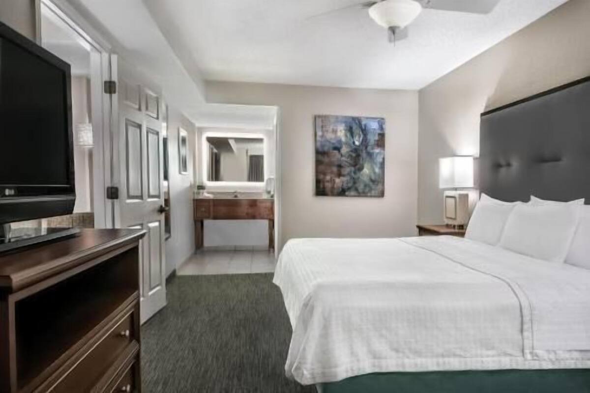 A hotel room with a bed, a TV, a bathroom, and a painting on the wall.