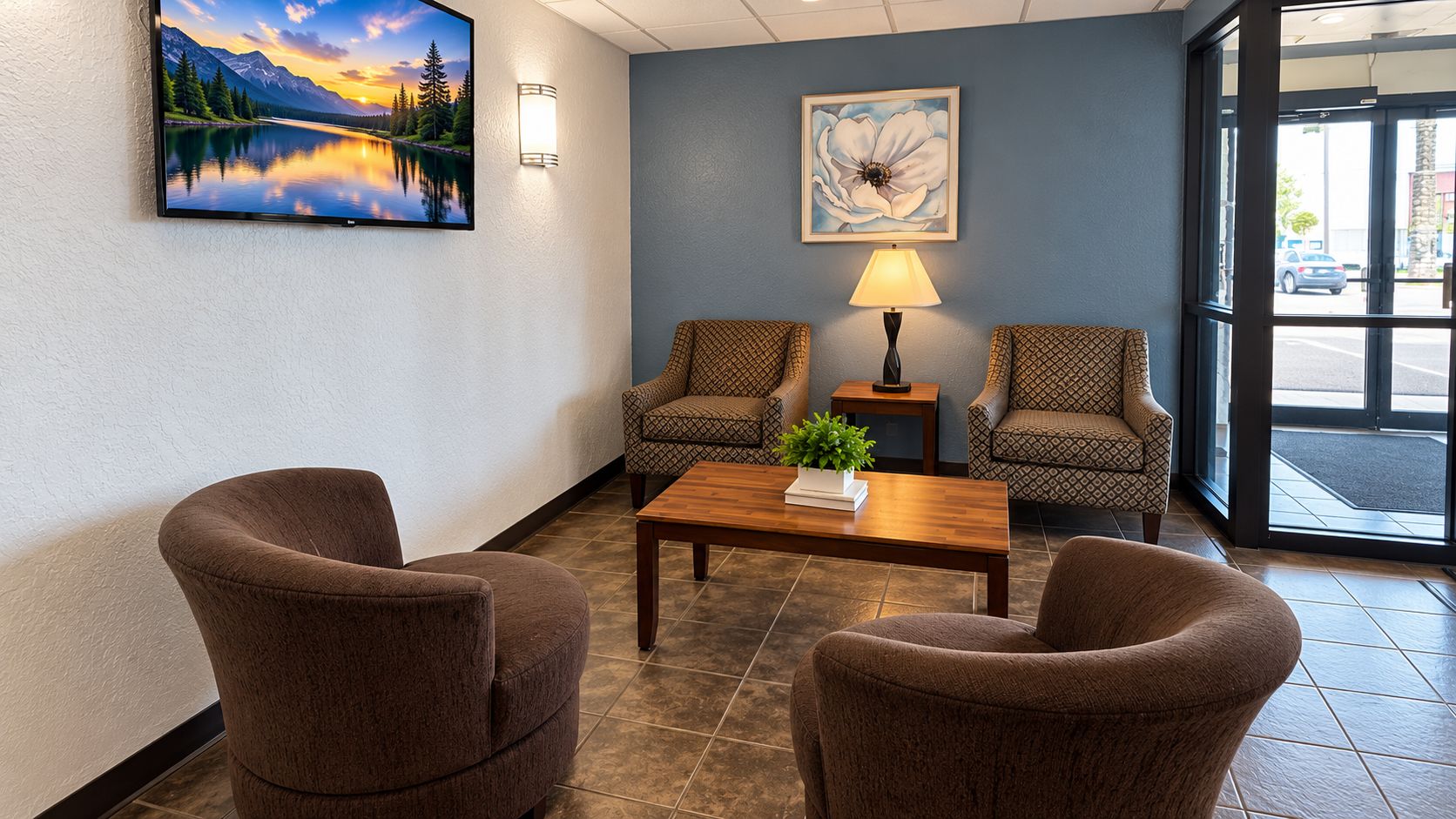 A lobby with two patterned armchairs, a wooden coffee table, a wall-mounted TV, a lamp, and a framed artwork.