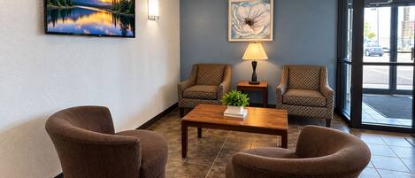 A lobby with two patterned armchairs, a wooden coffee table, a wall-mounted TV, a lamp, and a framed artwork.