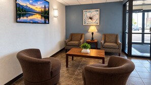 A lobby with two patterned armchairs, a wooden coffee table, a wall-mounted TV, a lamp, and a framed artwork.