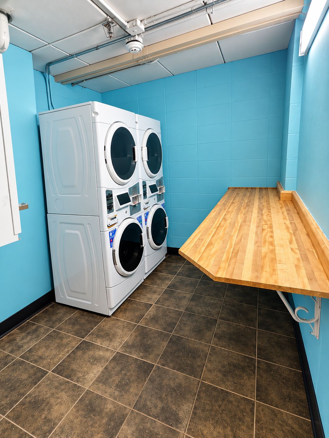 A laundry room with a stacked washer and dryer, a wooden bench, and blue walls.